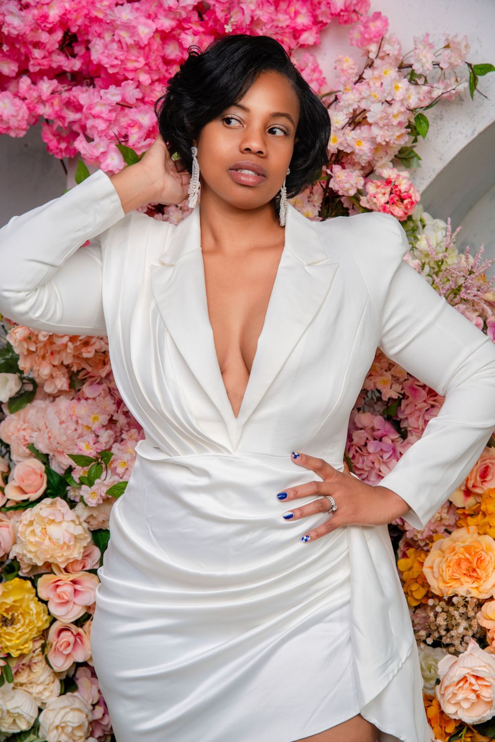 Elegant white blazer dress styled against backdrop of pink and peach floral arrangements in fashion photoshoot.