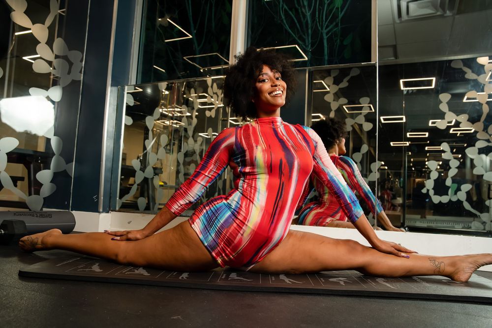 Athletic figure in a vibrant striped leotard performs a split pose in a modern fitness center.