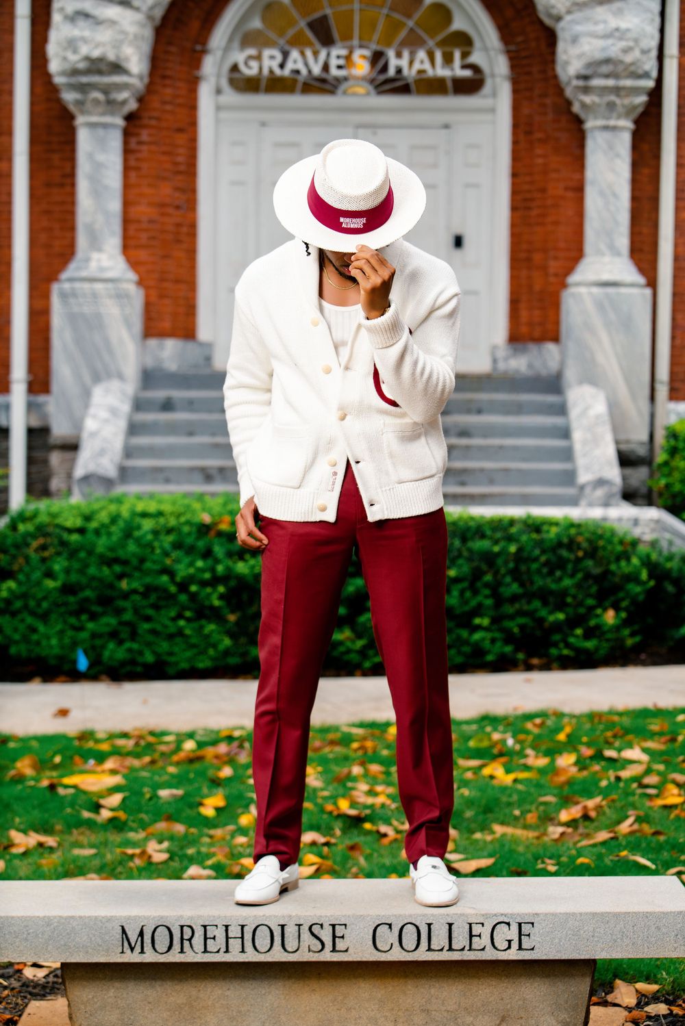 Student in white blazer and burgundy pants poses on Morehouse College sign outside Graves Hall.