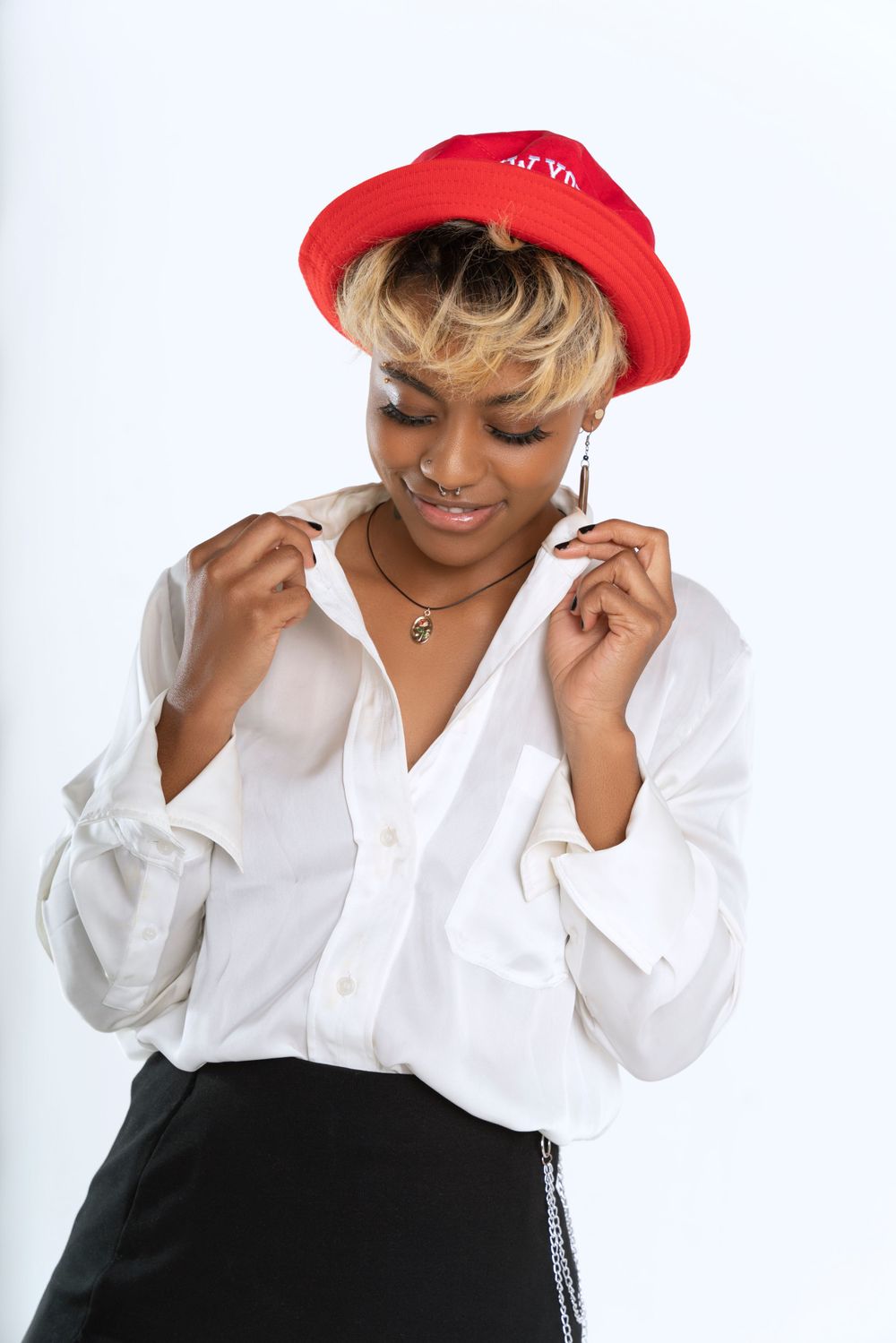 A person wearing a red cap and white button-down shirt smiles while looking down against a white background.