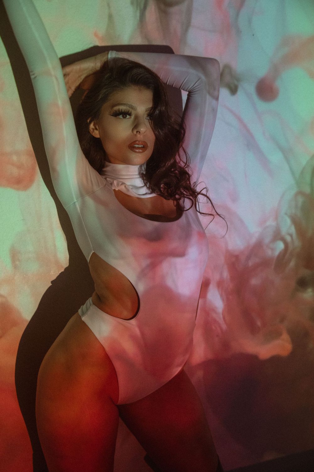 Artistic fashion portrait with dramatic lighting featuring smoke effects in teal and red tones.