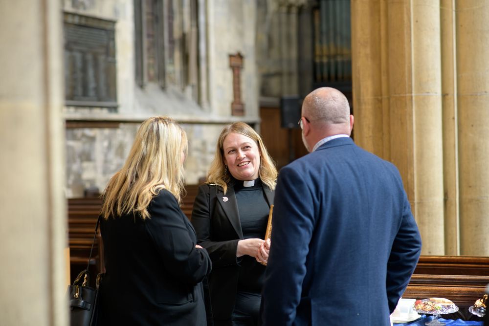 Three people having a conversation in front of a stone church or cathedral entrance.