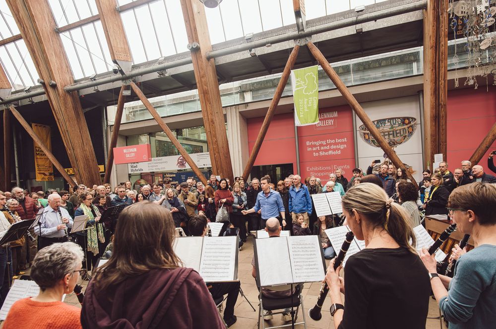 Large crowd gathered in an indoor venue with exposed wooden beams and glass ceiling during a public event.