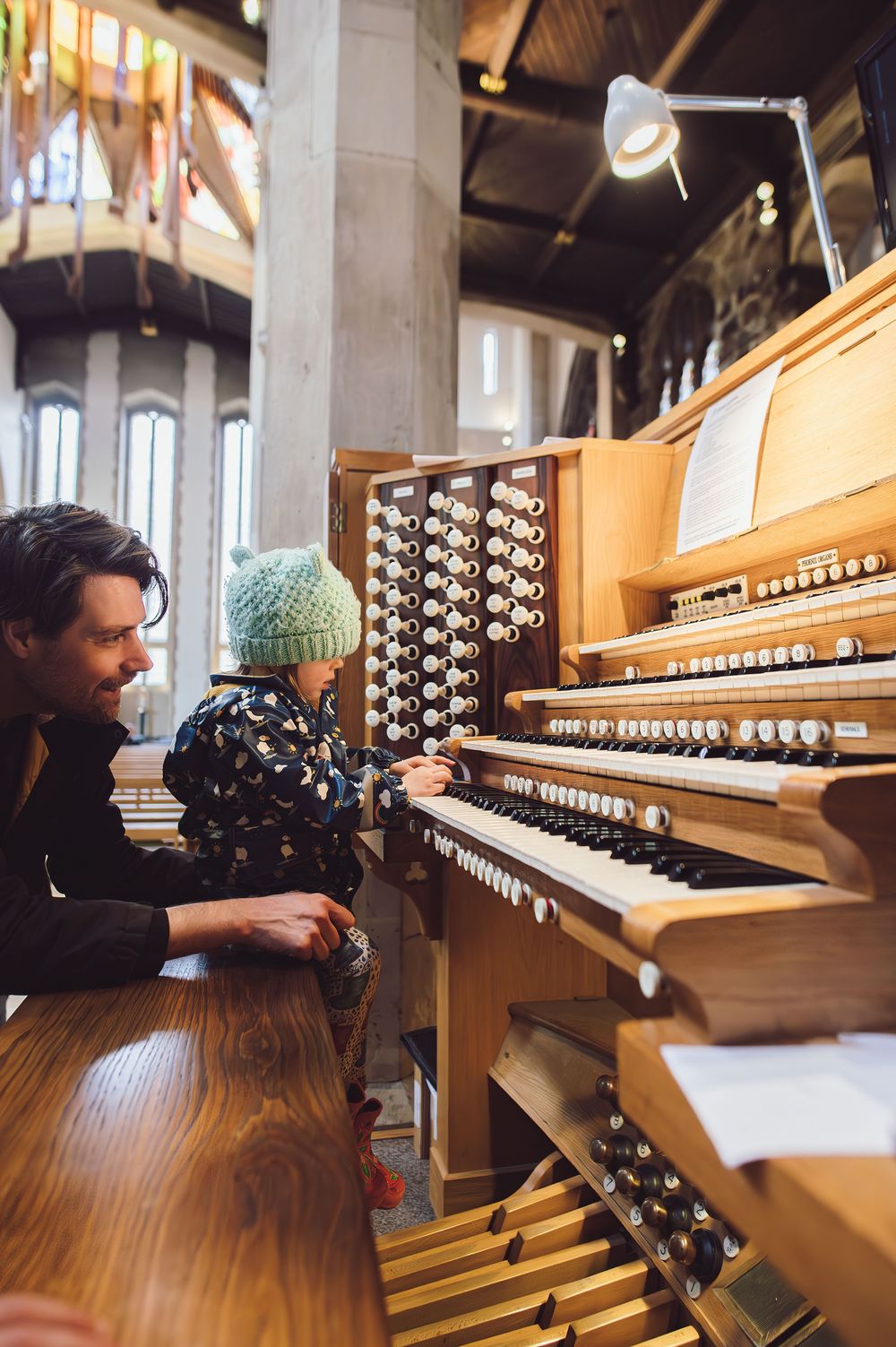 Two people sitting at a wooden church organ console examining the multiple keyboards and stops of the instrument.