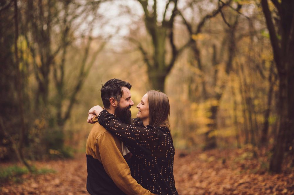 A couple embraces in an autumn forest surrounded by fallen leaves and bare trees.
