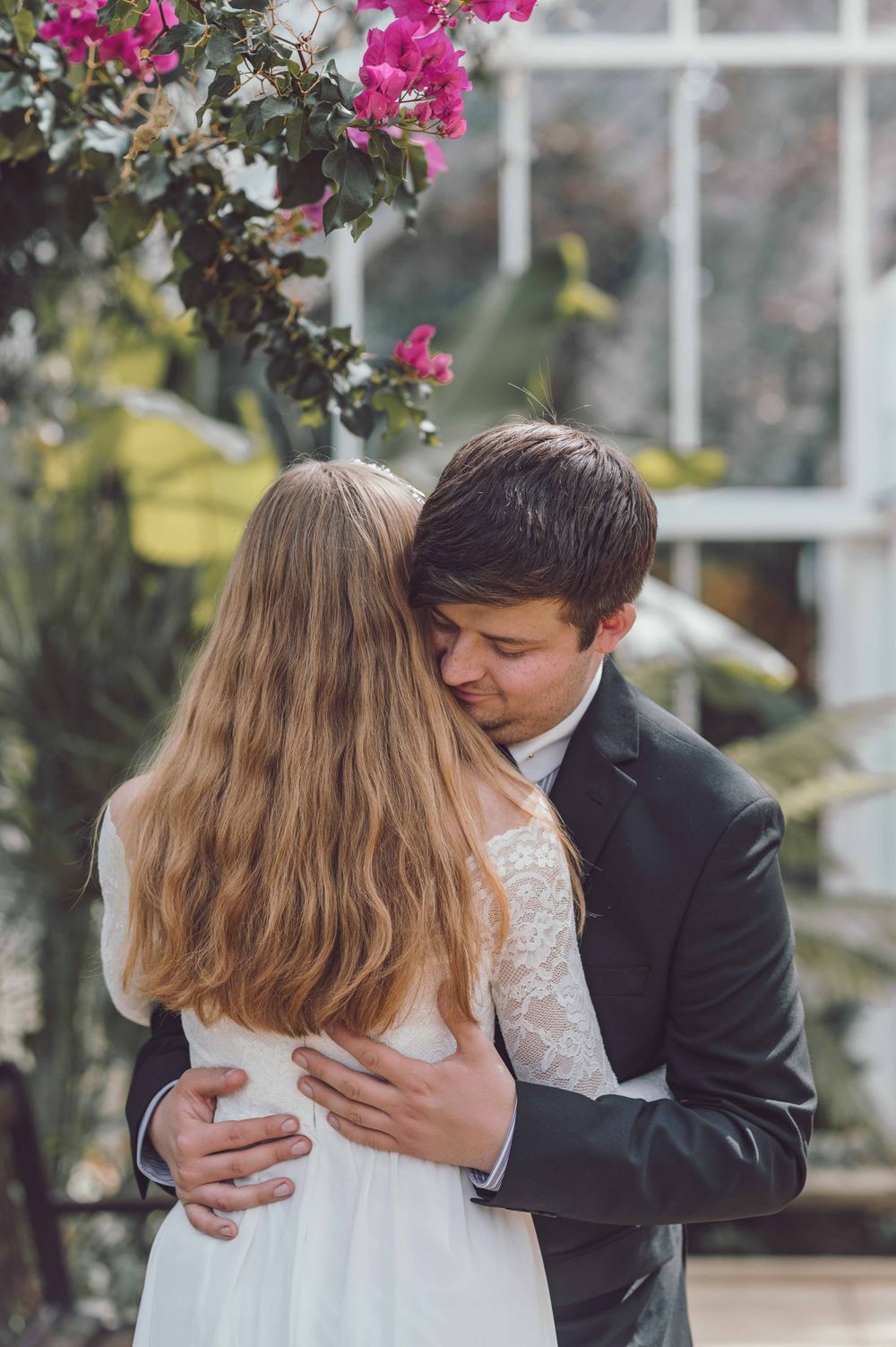 A romantic wedding moment captured in a greenhouse setting with pink bougainvillea flowers blooming overhead.
