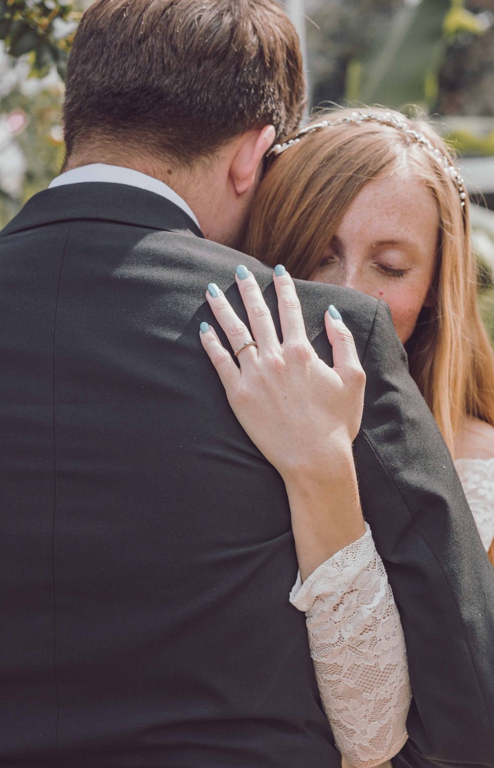 A romantic wedding moment showing a close embrace with the bride's hand displaying her new ring against the groom's suit.
