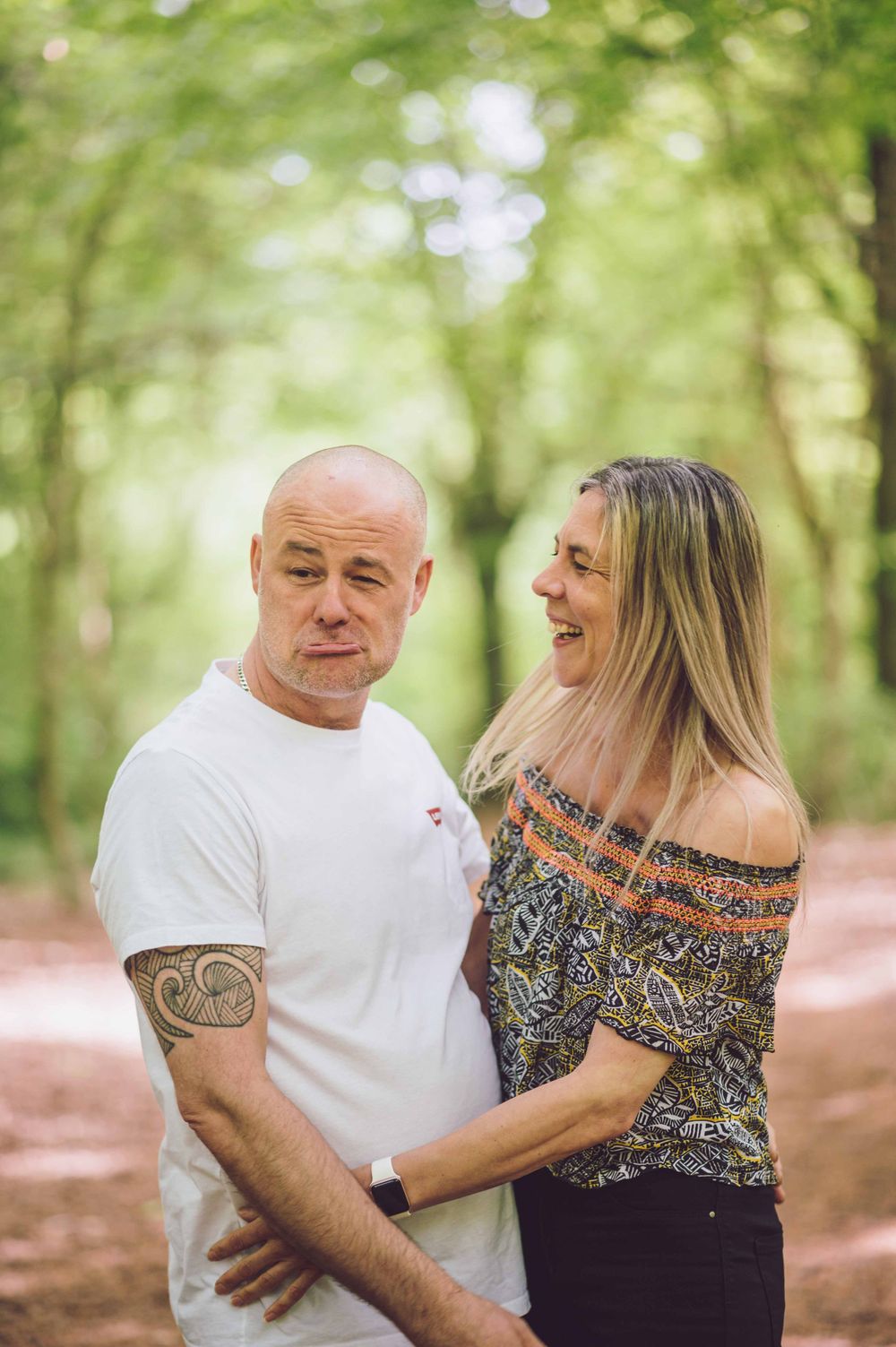 A couple shares a tender moment together in a sunlit wooded area on a nature path.