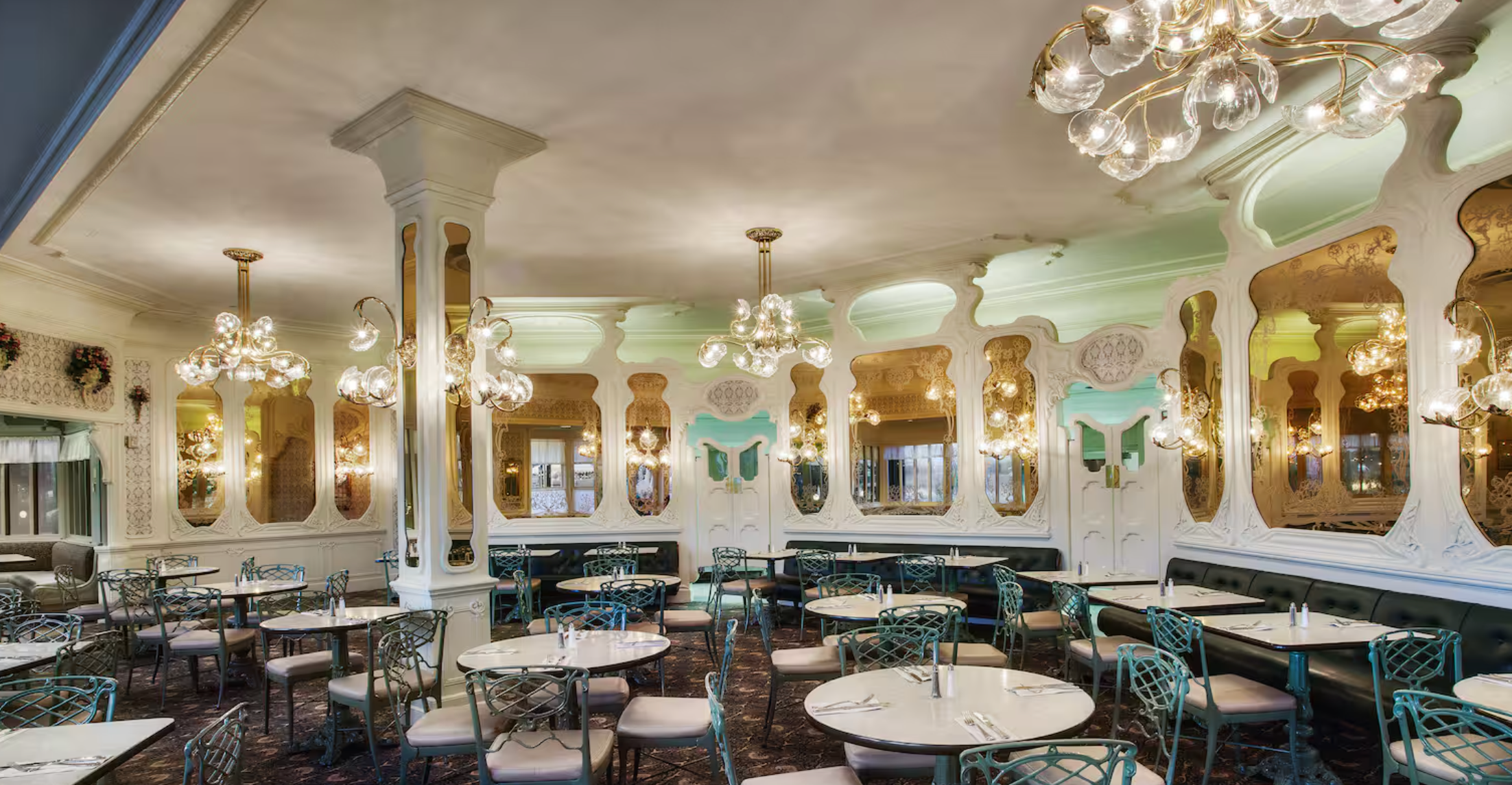 Elegant Victorian-style dining room with mint green walls, ornate columns, crystal chandeliers and round white tables.