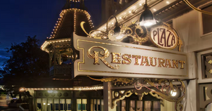 Illuminated restaurant signs and storefronts glow warmly along a nighttime street with twinkling lights.