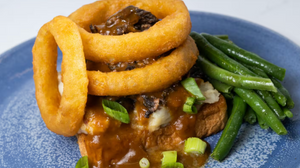 A plate of chicken marsala topped with crispy onion rings and served with steamed green beans in a rich brown sauce.