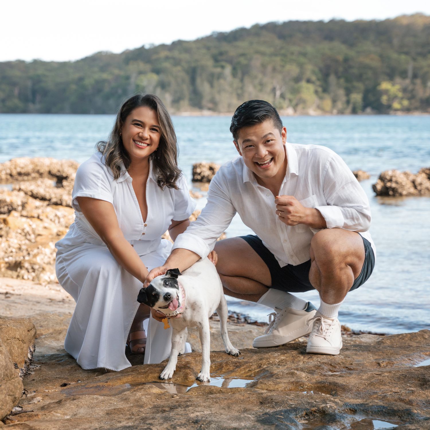 couple is petting their cute little dog on the rocks at Lilli Pilli Reserve in Sydney pet friendly couples photoshoot