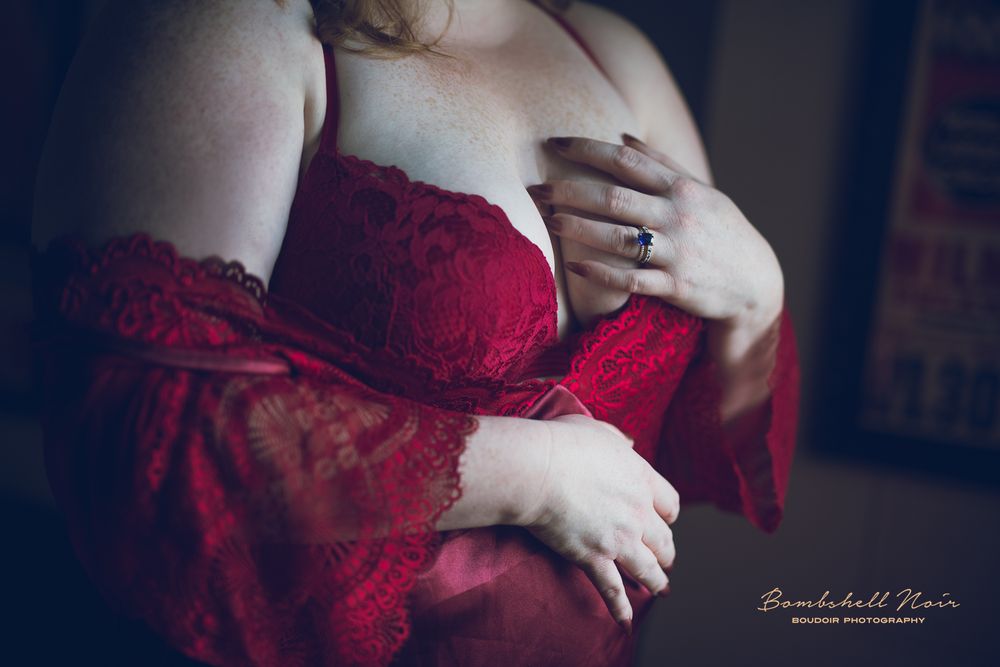 Close up photo of someone wearing a red lace boudoir outfit in moody lighting.