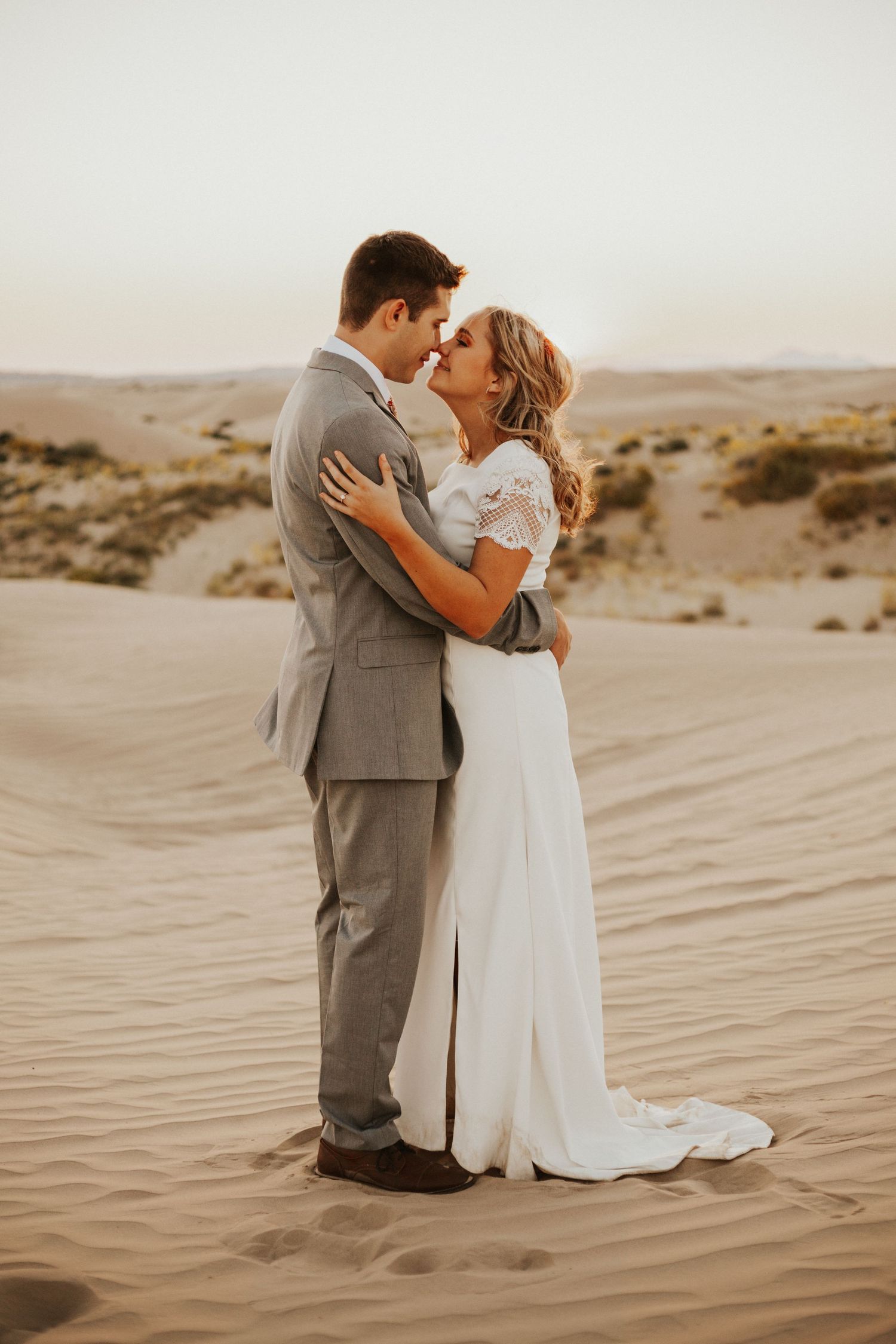 Bride and groom embracing on sand dunes at sunset in a desert wedding photo.