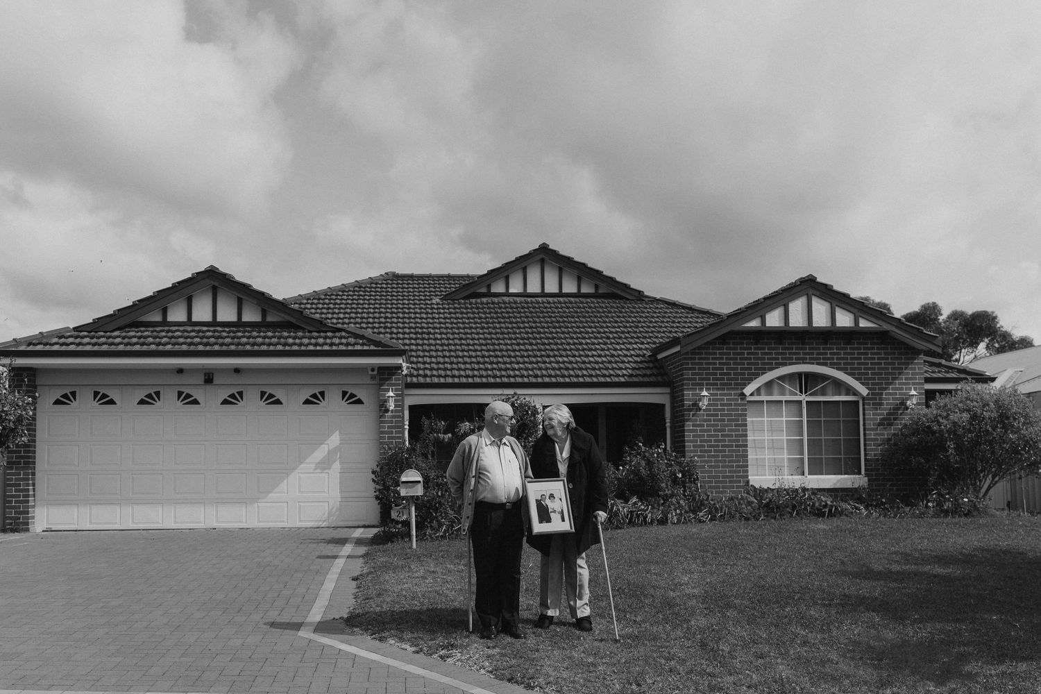 Family standing together outside their suburban single-story home with attached garage on a cloudy day.