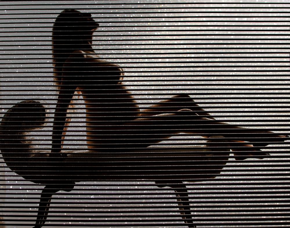 Maternity photoshoot and a silhouette of a pregnant woman resting on chaise against striped background.