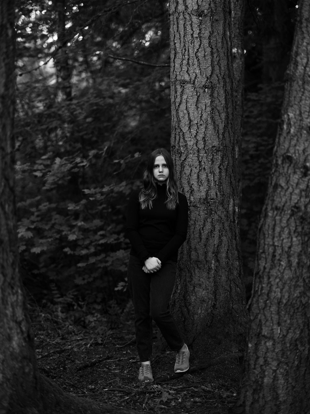 Moody forest portrait with subject positioned between two large tree trunks.