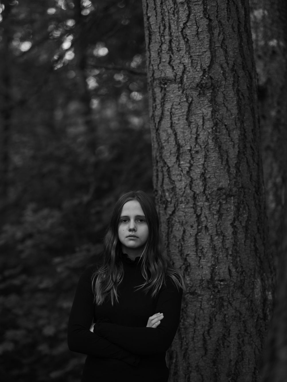 Minimalist black and white portrait next to large tree trunk in forest setting.