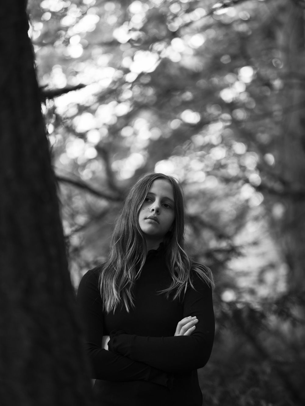 Atmospheric black and white portrait with bokeh lighting effects through forest trees.