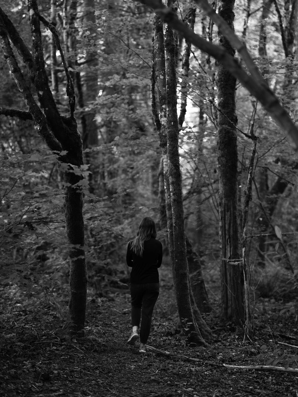 Figure in dark clothing walks through a misty forest path in black and white photography.