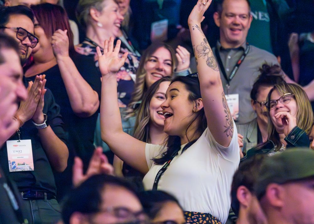 Excited crowd members cheer enthusiastically with raised arms during an event.