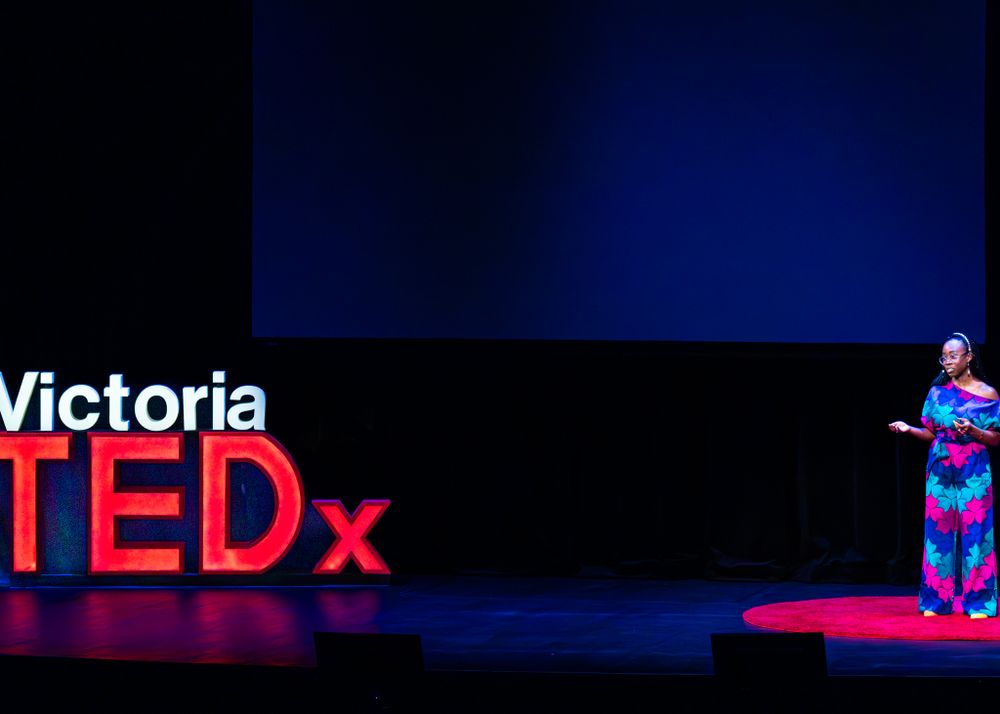 A speaker stands on a red circular TEDx stage against a dark background with the Victoria TEDx logo visible.
