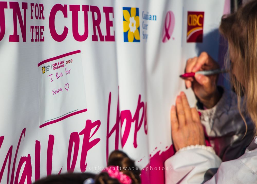 Someone writes on a pink and white wall labeled 'Wall of Hope' at what appears to be a cancer awareness event.