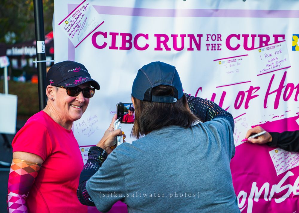 Runner in red shirt being interviewed at CIBC Run for the Cure charity event with pink banners visible in background.
