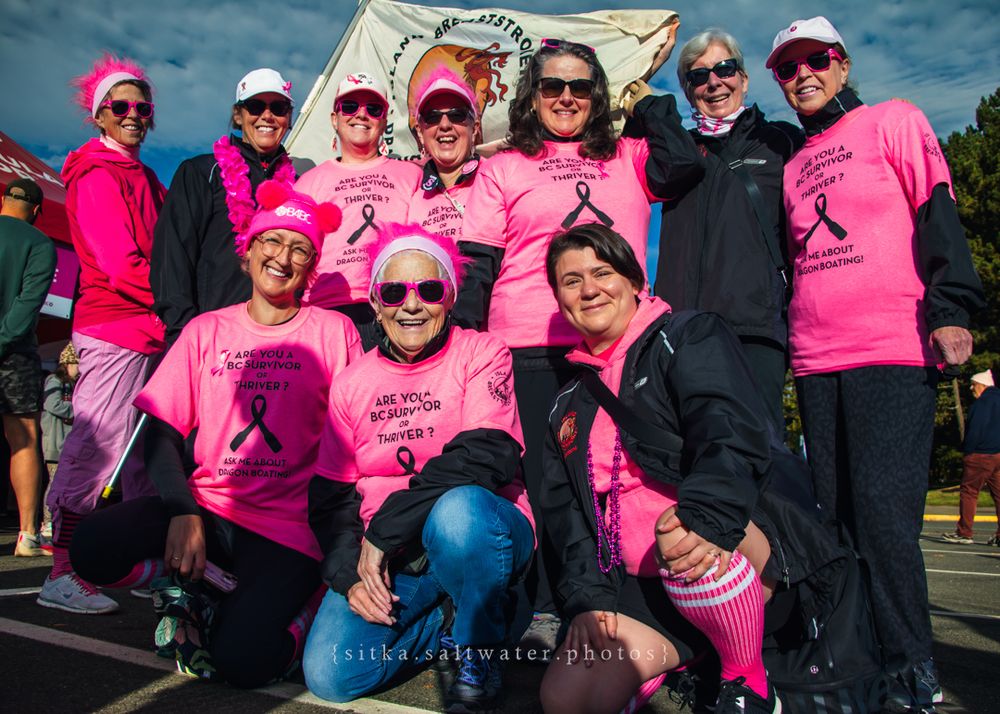 Group of participants wearing matching bright pink shirts and accessories gathered at an outdoor charity event.