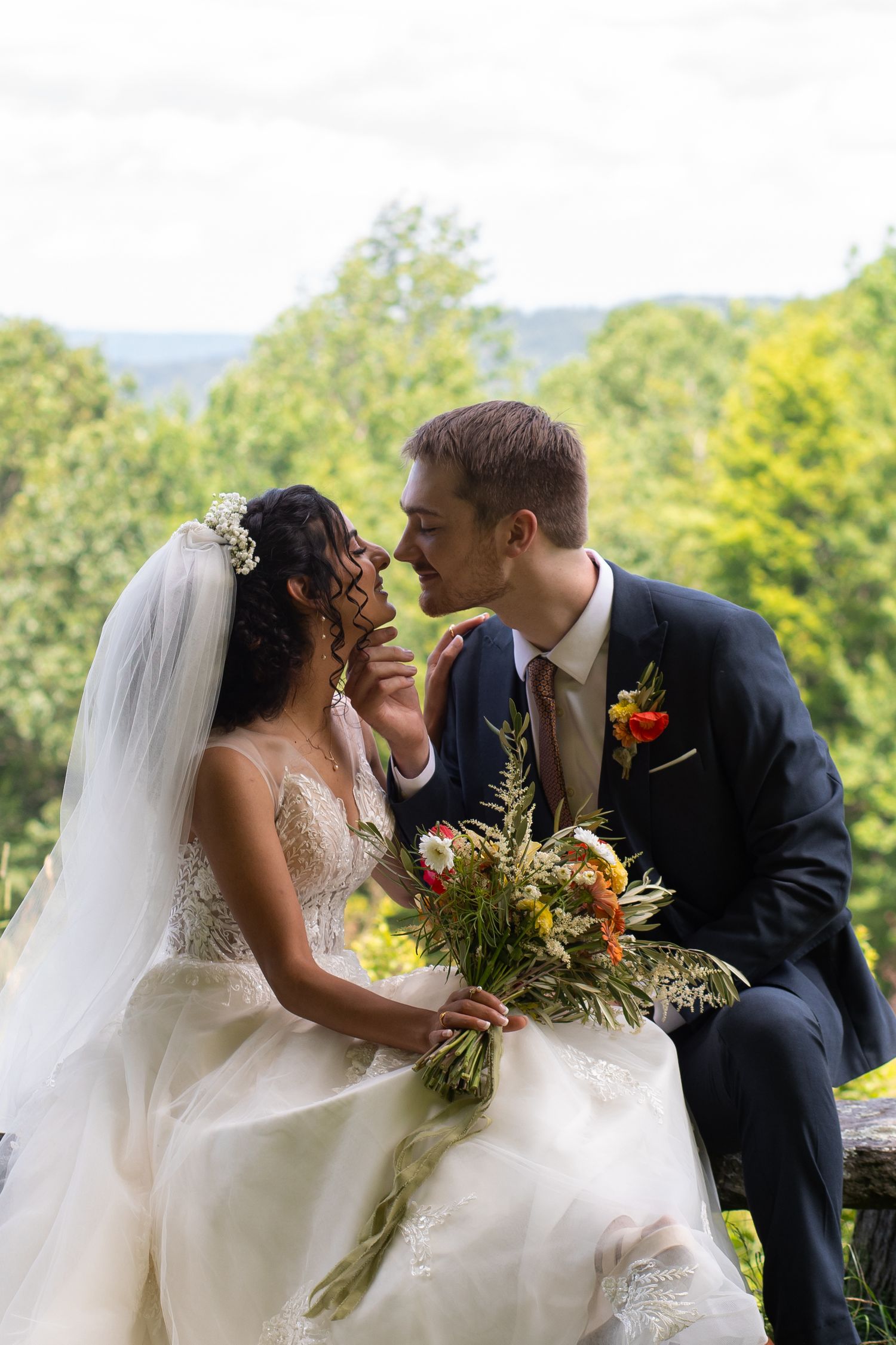 A romantic wedding moment with a beautiful floral bouquet against a backdrop of green trees and mountains between bride & groom.