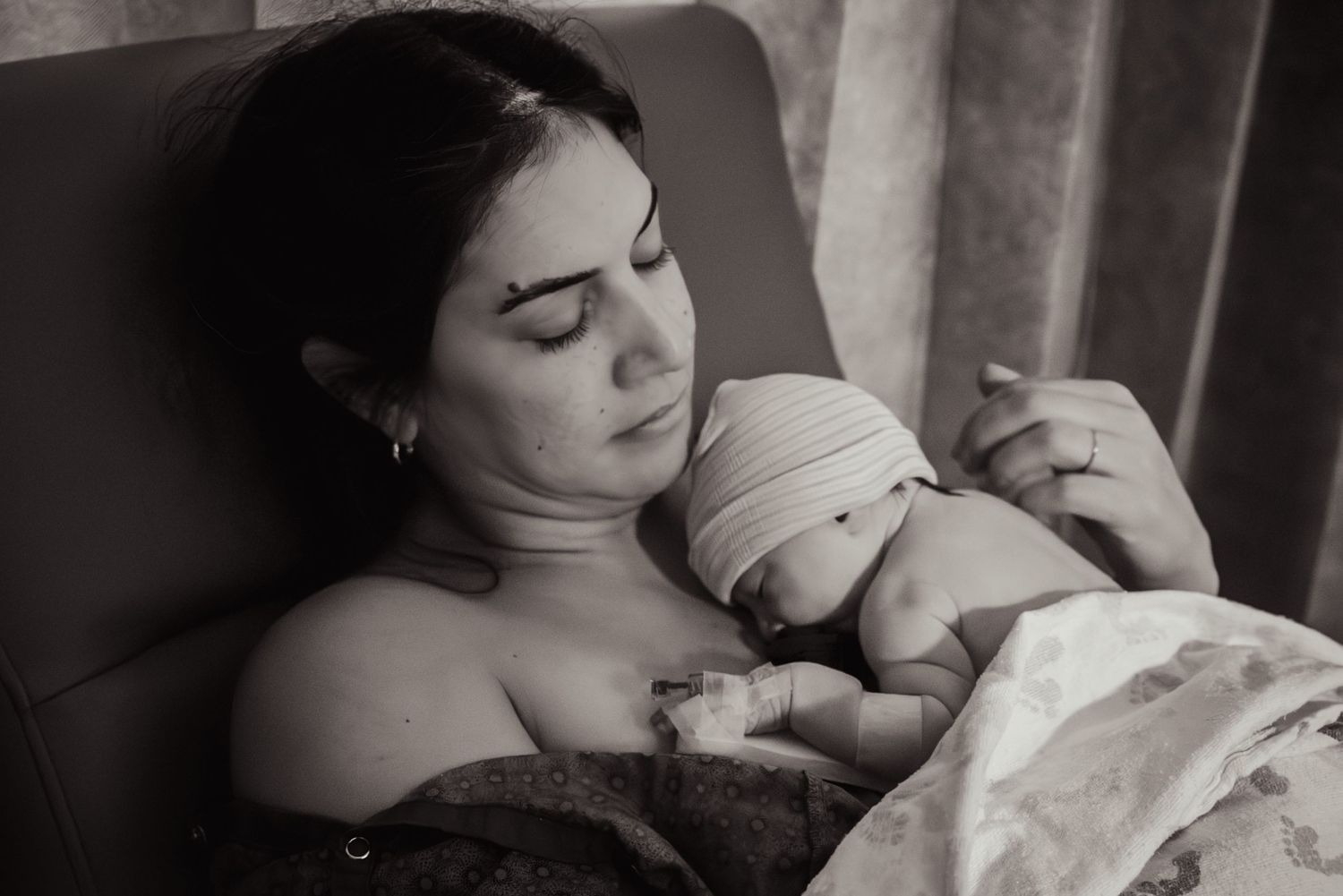 A black and white photo showing a tender intimate moment between mother and baby after a c-section birth.