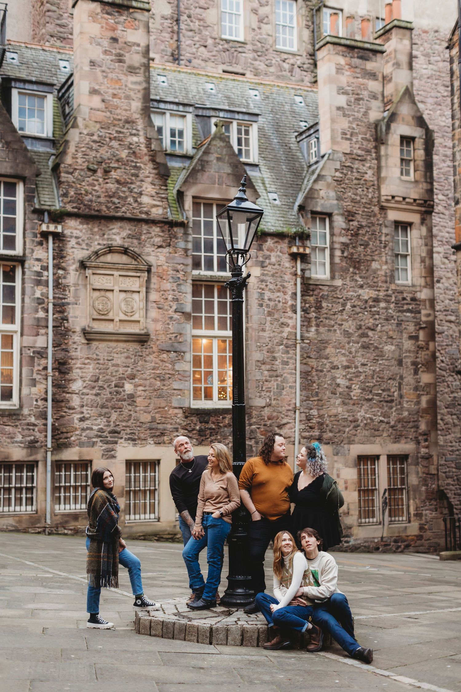 Groups of people gather and socialize in a historic stone courtyard with traditional architecture and windows.