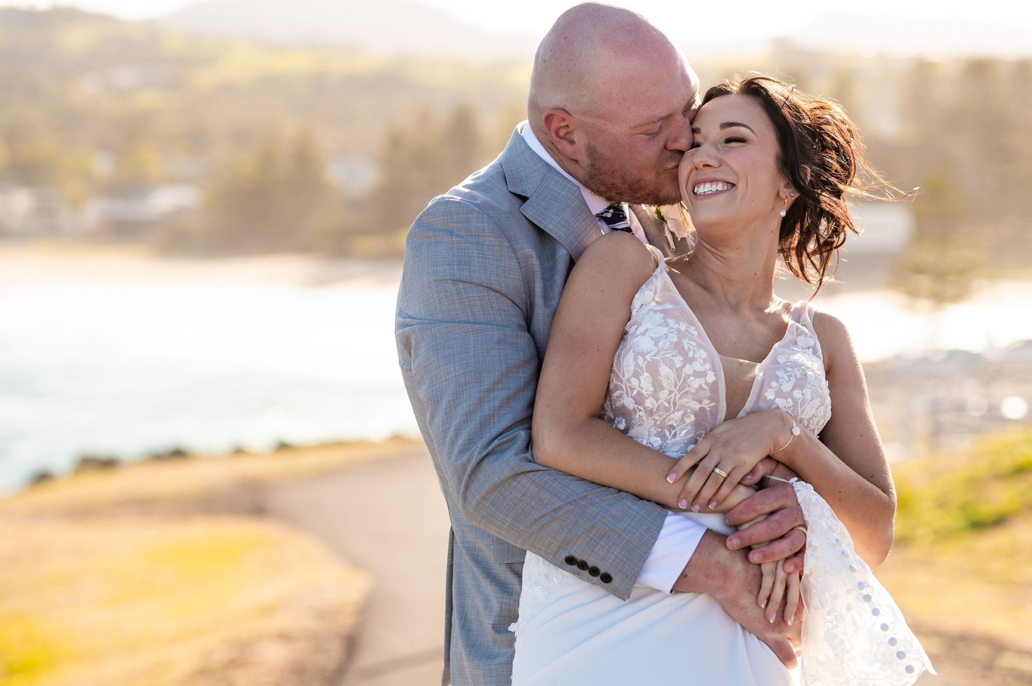 Couple embraces on sandy beach at sunset as gentle waves roll onto shore during romantic photoshoot.
