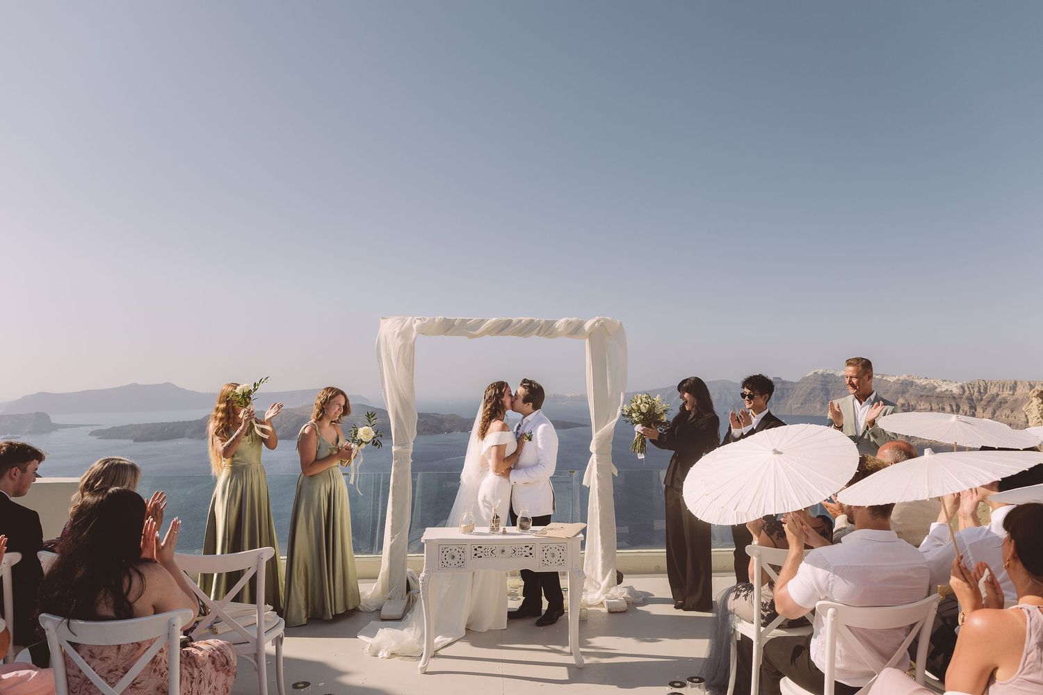 A couple kiss at their destination wedding ceremony at Santorini while their guests applaud.