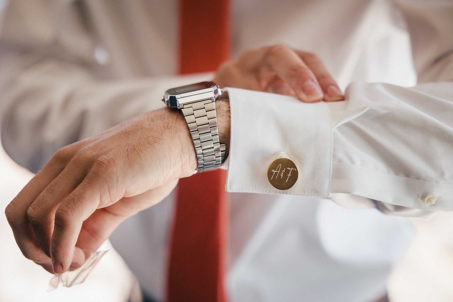 Close-up of groom adjusting monogram cufflinks and watch during Boston wedding preparations
