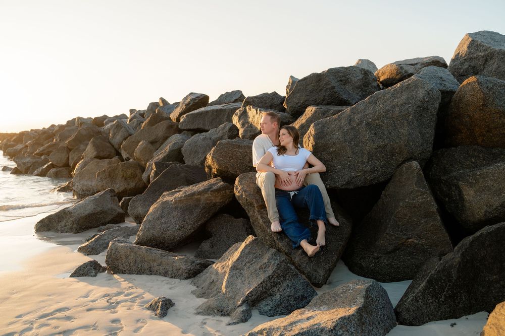 Couple sitting together on rocky beach cliffs during golden hour sunset.