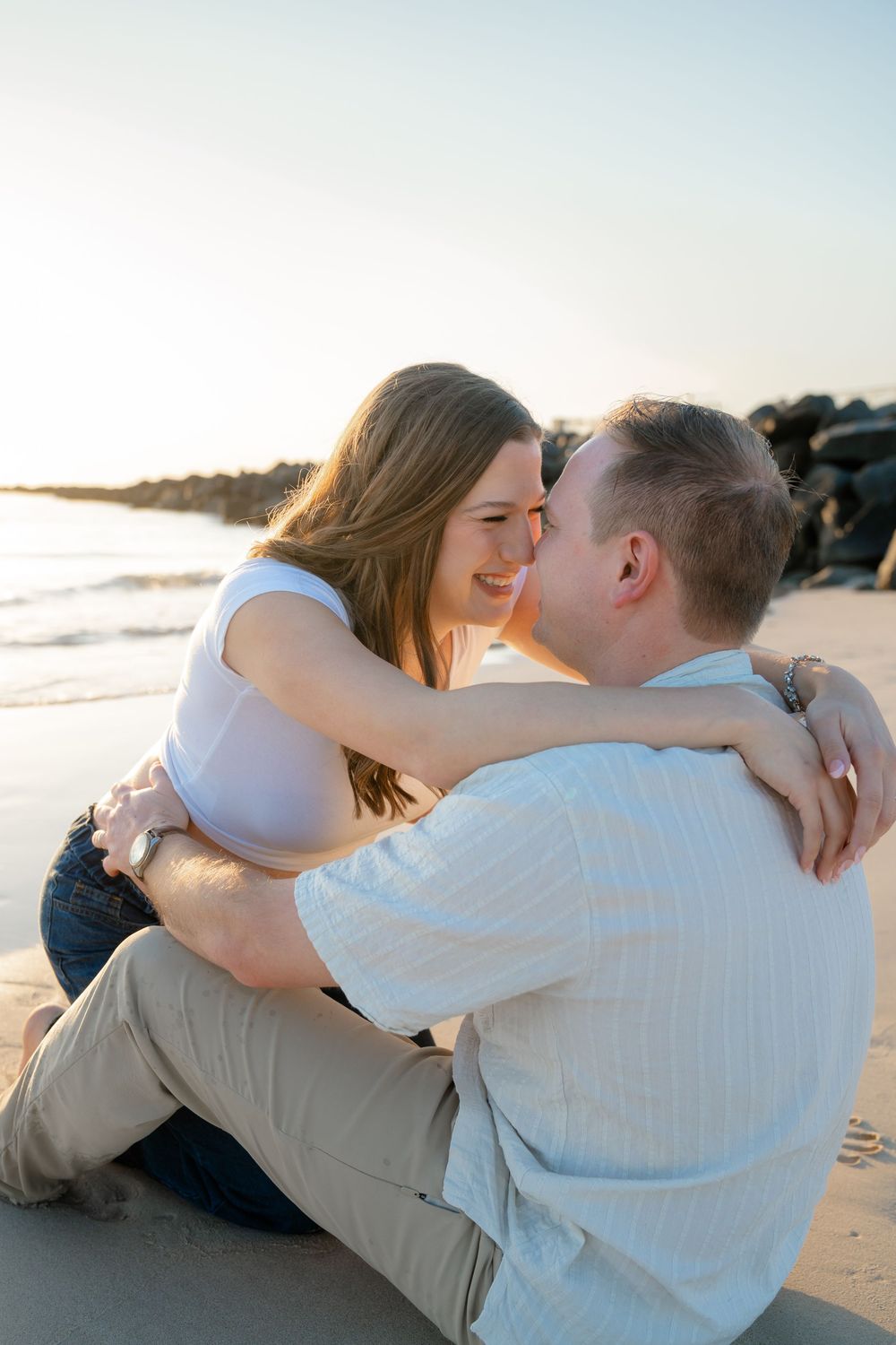 A romantic couple shares tender moments while laying on a sandy beach at sunset.