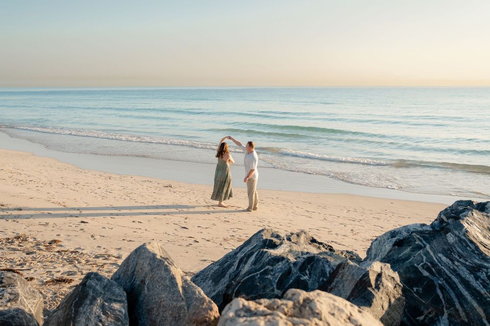 Couple walking along a serene beach at sunset with waves gently rolling onto the sandy shore.