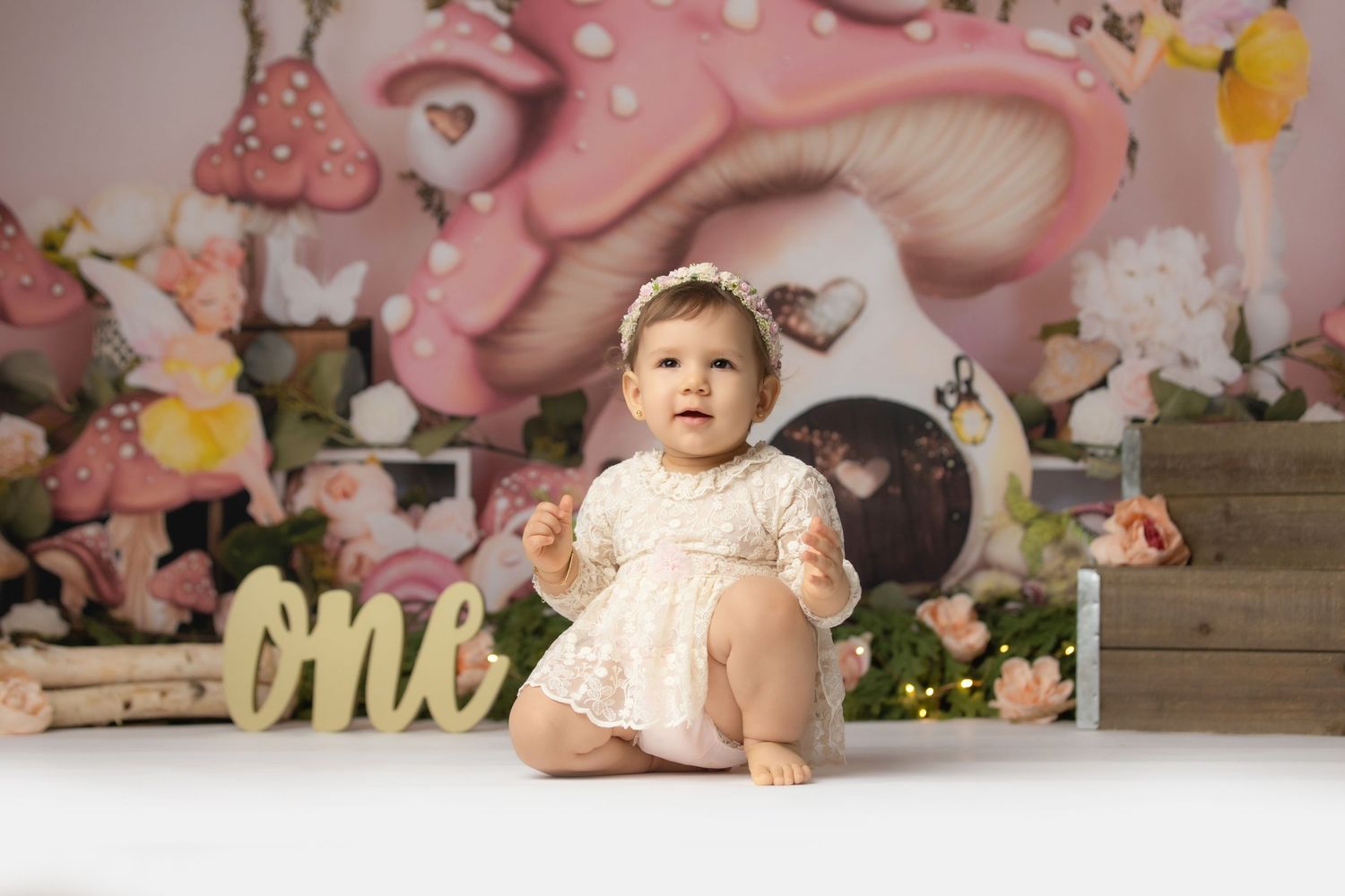 A pink and floral themed first birthday cake smash photo session with decorative elements and props.
