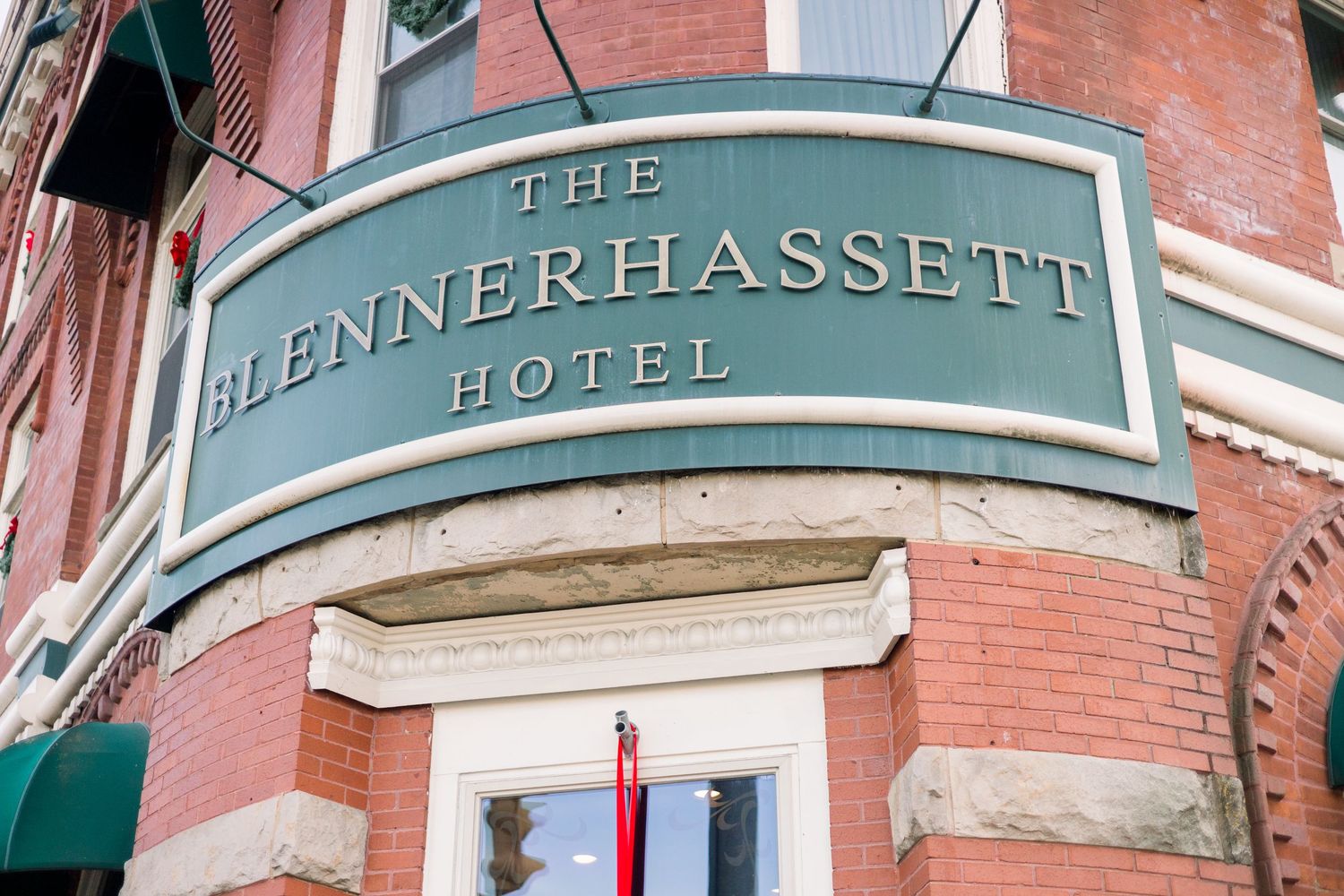 Historic brick building facade with green awnings and ornate signage for The Hotel Blennerhassett in downtown setting.