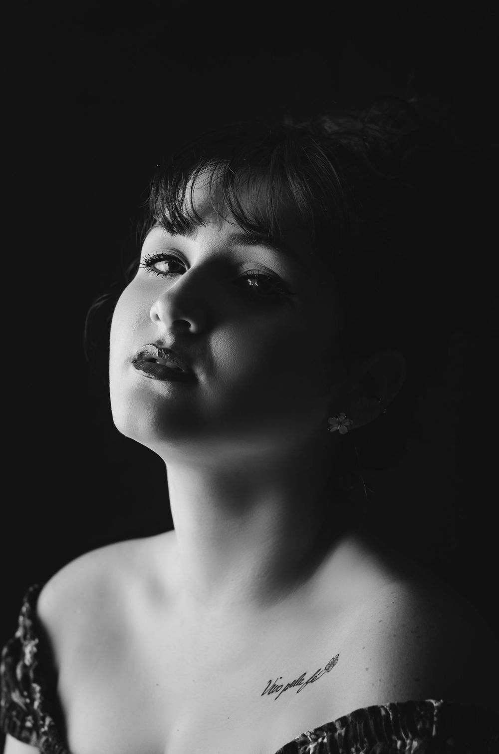 Retrato feminino em fotografia low key preto e branco. Modelo com tatuagem e iluminação dramática em estúdio. Ensaio artístico.