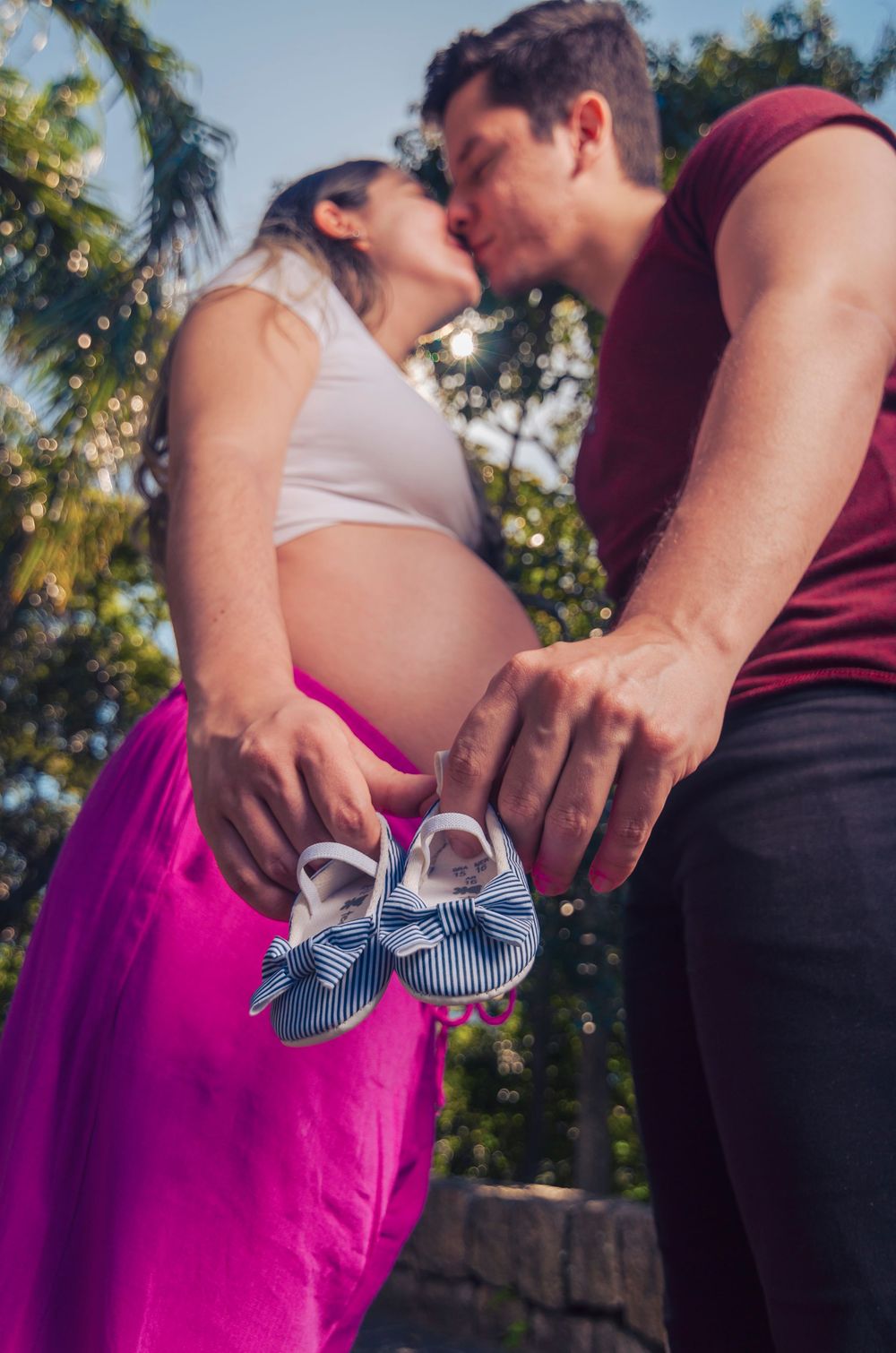 Ensaio gestante no Leme, Rio de Janeiro. Casal se beijando com destaque para a barriga e sapatinhos de bebê. Fotografia de família externa.