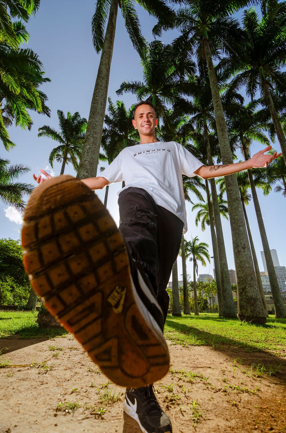 Retrato criativo masculino com pose dinâmica em contra-plongée. Fotografia artística em parque com palmeiras.