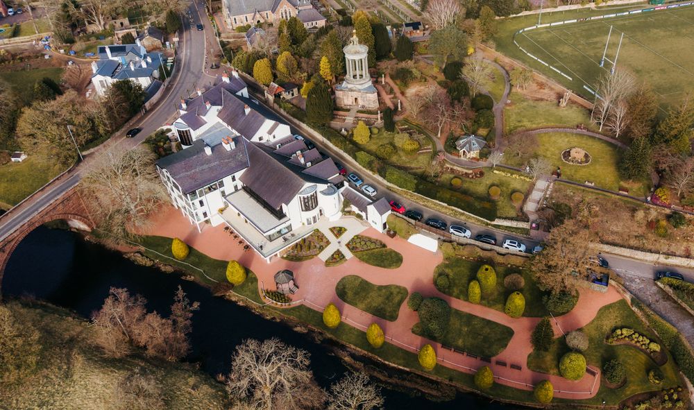 Aerial panoramic view of a coastal town with buildings and roads nestled among autumn trees.