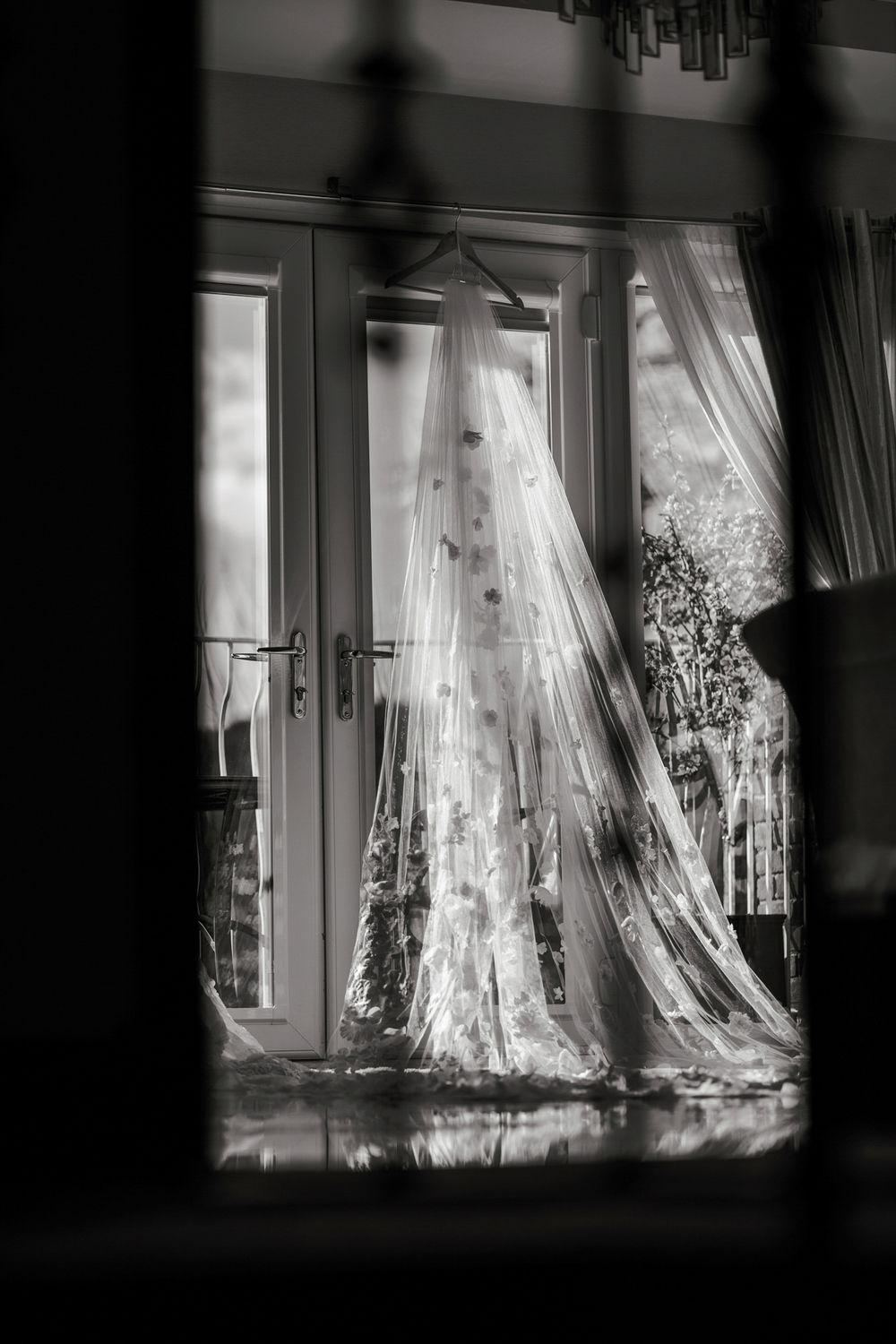 Ethereal white curtains billow in front of sunlit windows creating a dreamy, romantic atmosphere in black and white.