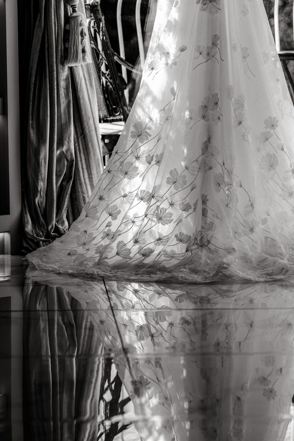 Close-up details of a delicate white wedding dress train with floral embroidery and lace patterns reflecting on a glossy floor.