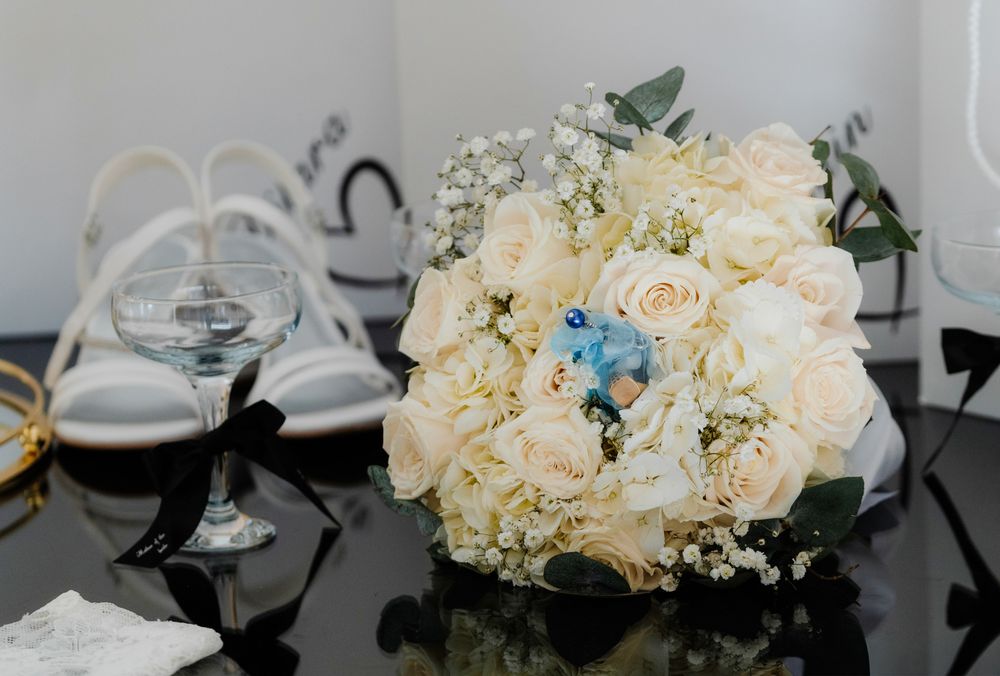 Elegant white and cream wedding bouquet with roses and blue accents arranged on a reflective surface.