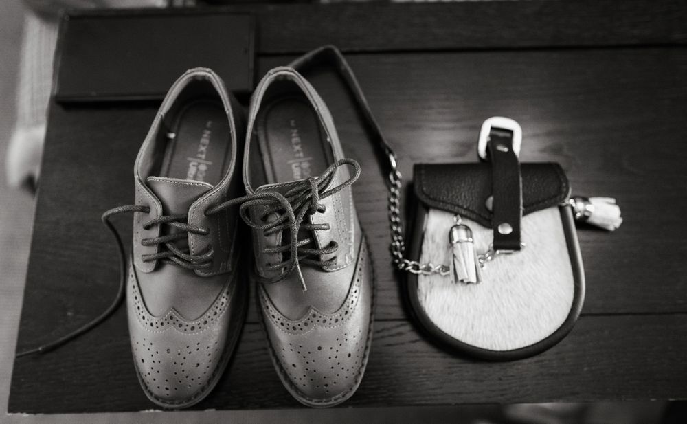 Black and white image showing a row of leather dress shoes and boots arranged on a dark surface.