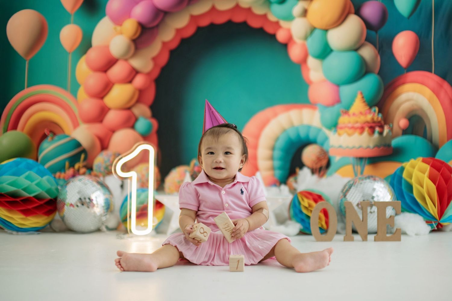 Colorful balloon decorations and props arranged for a baby's first birthday cake smash photo session against teal backdrop.