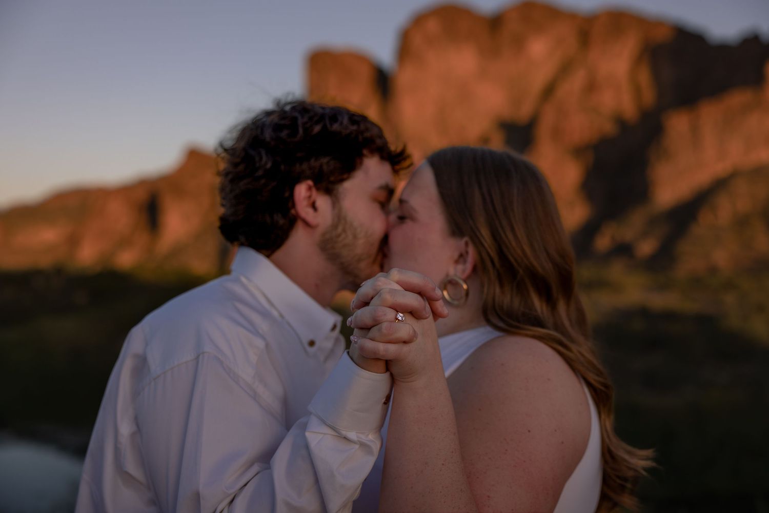 Couple sharing a tender kiss at sunset with glowing red rock mountain backdrop in Arizona.